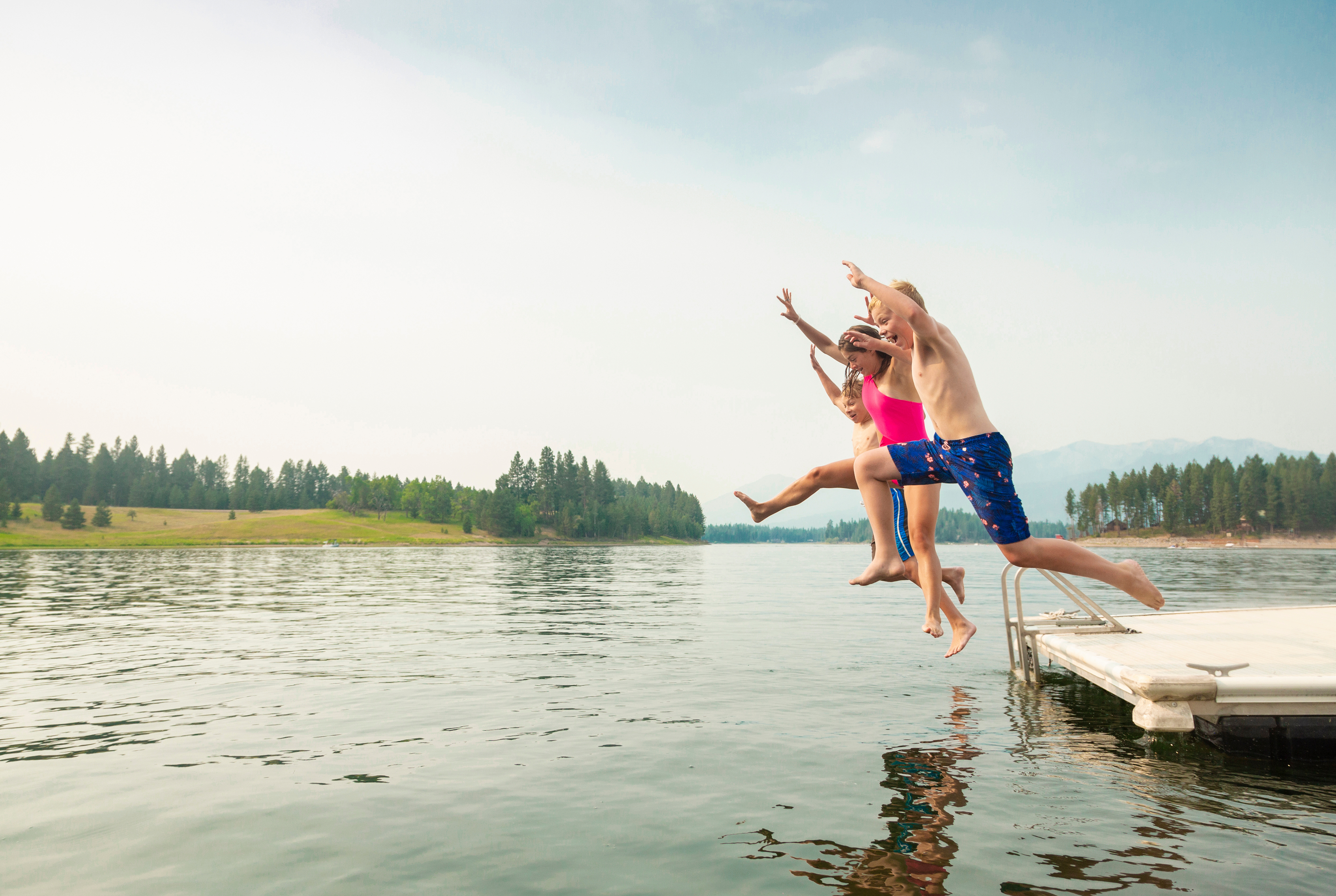 Group of kids jumping off a dock into the lake together