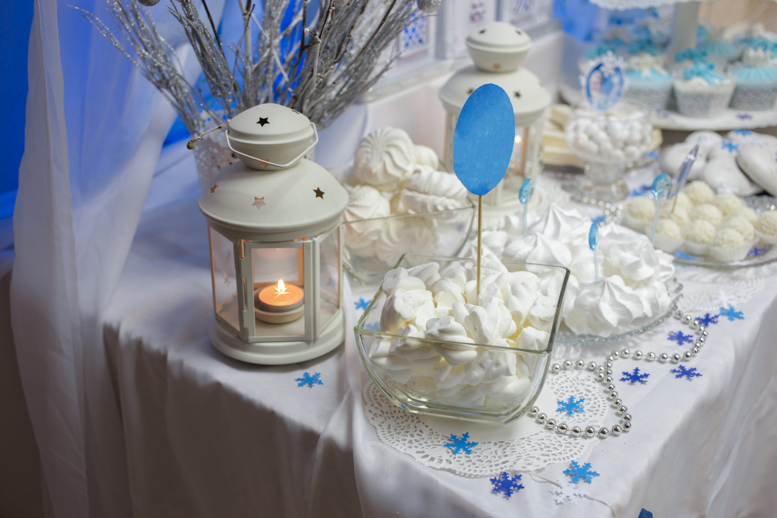 Festive table with sweets in a white color scheme. Side lit lantern with a candle.