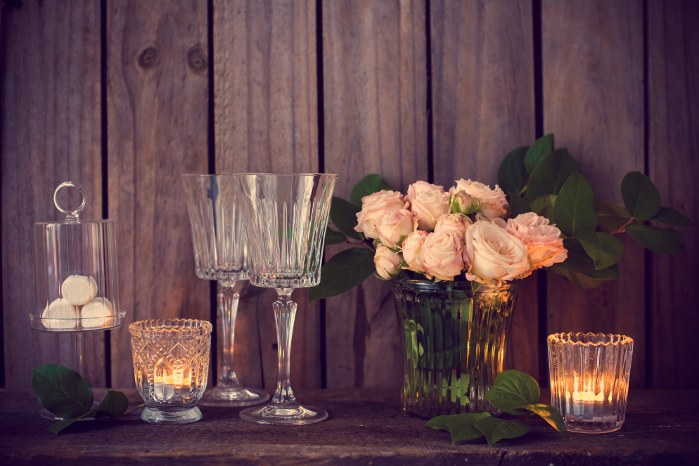 A table set with wine glasses, a candle, and a vase of pink roses